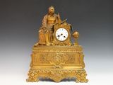 une horloge en or surmontée d'une statue représentant un homme assis