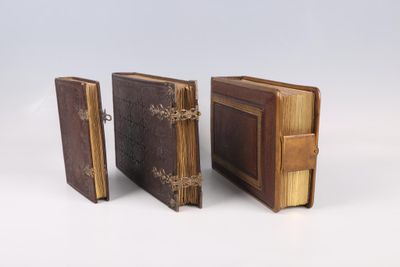 trois livres reliés en cuir, empilés les uns sur les autres sur une surface blanche