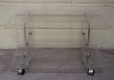 une table en verre transparent munie de roulettes, posée sur un sol en béton