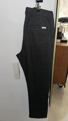 grey pants hanging on a hanger in a room with a white wall