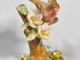 a figurine of a bird sitting on a branch with flowers