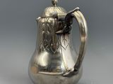 une cafetière ancienne en argent avec une anse, sur fond gris