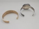 two silver and gold cuff bracelets on a white surface