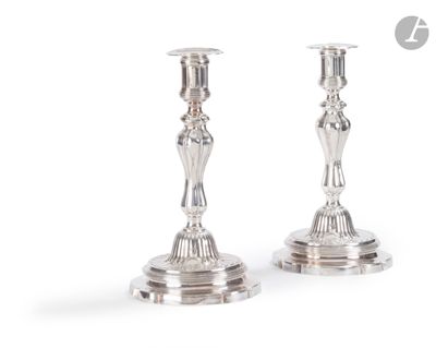 une paire de bougeoirs en argent posés sur une surface blanche