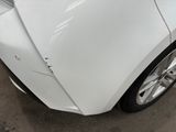 the front end of a white car with a denting dent on it