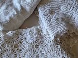 a pile of white crocheted sweaters on a bed