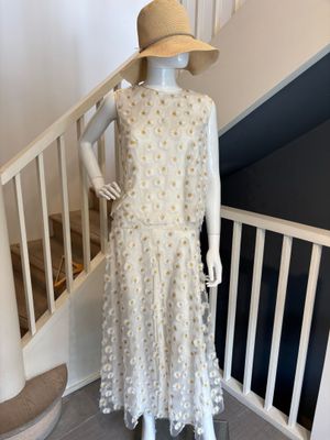 Le mannequin porte une robe blanche et un chapeau de paille.