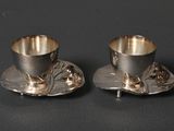 pair of silverplated cups and saucers on a black surface