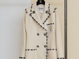 beige jacket with black buttons on a hanger in front of a beige wall