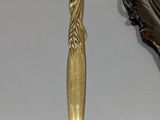 a gold spoon next to a bronze spoon with a feather on it