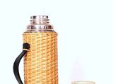 a wicker coffee pot next to a stainless steel cup