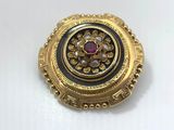 a close up of a gold and black broochle on a white surface