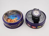 purple tin with a watch inside of it sitting on a white surface