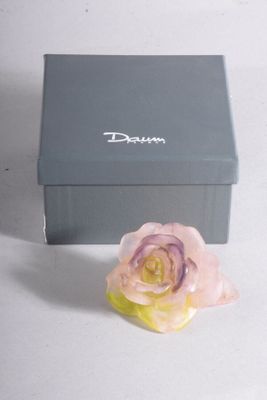 une petite rose rose posée devant une boîte grise