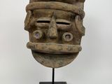 un masque en bois posé sur un socle noir, sur fond blanc