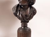 bronze bust of a woman with a hat on a pedestal