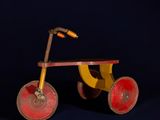 tricycle en bois jaune et rouge sur fond bleu foncé