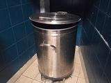 a metal trash can in the corner of a bathroom