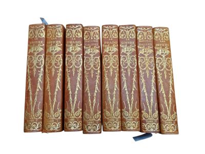six old books are lined up in a row on a white surface
