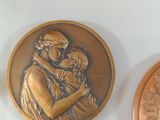three bronze medallions depicting a woman holding a baby and a man holding a dog
