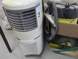 a small air conditioner sitting on the floor next to a pile of bags