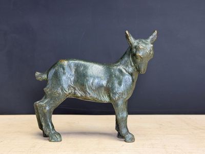 statue en bronze représentant une chèvre, posée sur une table en bois devant un mur noir