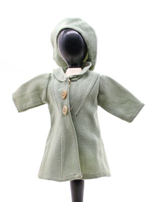 une poupée qui porte un manteau vert et un chapeau