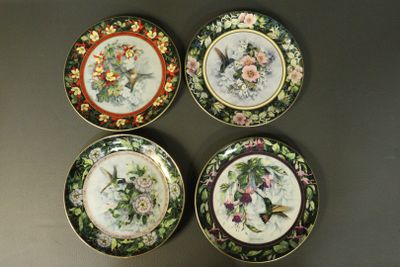 quatre assiettes ornées d'oiseaux et de fleurs, posées sur une table