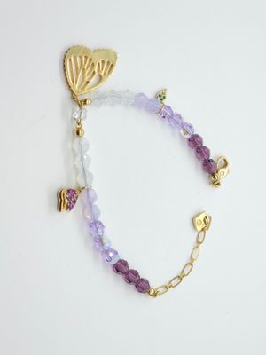 un gros plan d'un bracelet posé sur une surface blanche, orné d'une breloque en forme de papillon doré