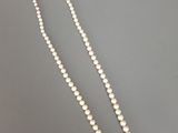 un collier de perles blanches muni d'un fermoir en argent, sur fond gris