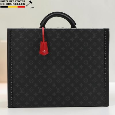 une mallette Louis Vuitton noire avec une poignée rouge, posée sur une table blanche