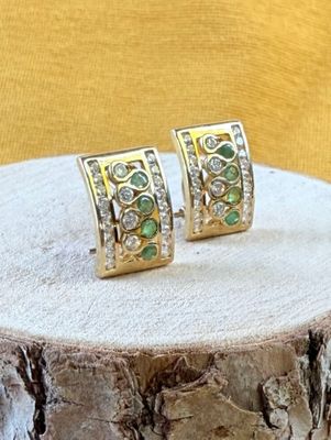 une paire de boucles d'oreilles en émeraude et diamant posée sur une souche d'arbre