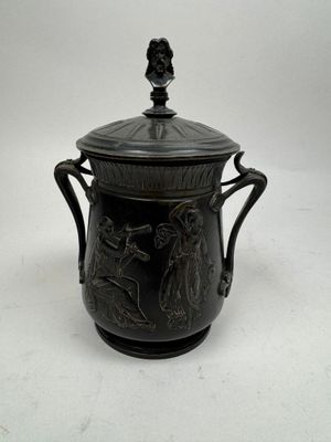 un vase noir muni d'un couvercle, posé sur une surface blanche