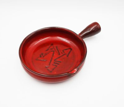 an old red bowl with writing on it sitting on a white surface