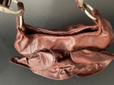 brown leather purse hanging on a hook on a gray surface