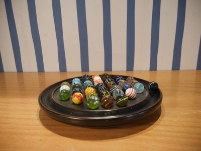 un bol rempli de billes posé sur une table, avec un mur rayé en arrière-plan