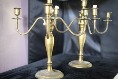 deux chandeliers en or posés sur une table, avec une horloge en arrière-plan
