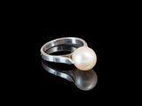 une image représentant une bague en perle blanche posée sur une surface noire