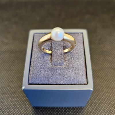 un gros plan d'une bague en or sertie d'une perle blanche