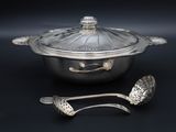 a silver pot with a lid and two spoons next to it