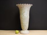a white vase sitting on a table with a green apple in front of it