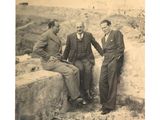 trois hommes assis sur un mur de pierre, dont l'un tient sa main