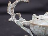 a small metal teapot with a bird decoration on top of it
