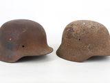 pair of wwii era german steel helmets on a white background