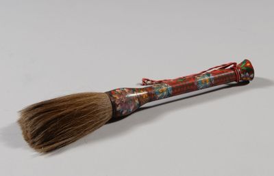 un gros plan d'un pinceau posé sur une surface blanche, avec un manche rouge