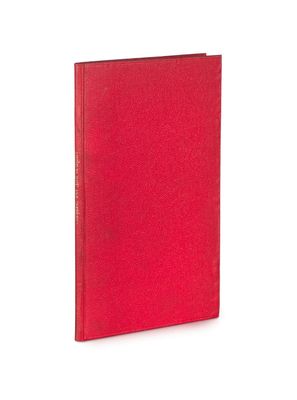 un livre rouge posé sur une table blanche à côté d'un mur blanc