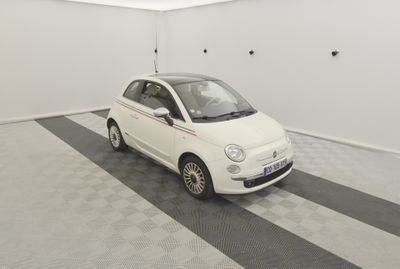 une Fiat blanche garée dans un garage dont le sol est recouvert d'un motif à carreaux noirs et blancs