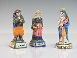 three ceramic figurines of three people standing next to each other on a white surface
