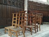 Plusieurs chaises en bois sont alignées dans une pièce dont un mur est recouvert de lambris.
