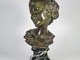 un buste antique en bronze représentant une femme aux cheveux bouclés, posé sur un socle en marbre